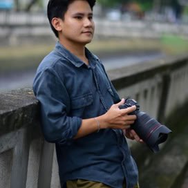 Young male photographer in casual attire holding a camera outdoors.